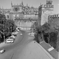 Vista desde la Puerta del León del Alcázar. En la plaza del Triunfo se observa el aparcamiento de vehículos ante el monumento al Triunfo y la Cruz de los Caídos adosada a la muralla del Alcázar. ca. 1965. ©ICAS-SAHP, Fototeca Municipal de Sevilla, fondo Serrano