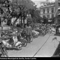 Guardias en el  aparcamiento de motos y bicicletas de la Plaza del Duque de la Victoria. Se aprecian los Almacenes del Duque en el palacio del marqués de Palomares, las obras en la iglesia de San Hermenegildo y la tienda de electrodomésticos Ortega. 1961. ©ICAS-SAHP, Fototeca Municipal de Sevilla, fondo Cubiles