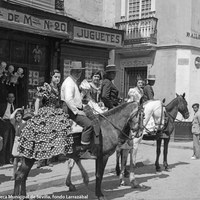 Caballistas con flamencas a la grupa se dirigen al Real. Posan en la calle Bailén esquina con Pedro del Toro, ante la juguetería de Vda. de Martínez. 1935 ca.