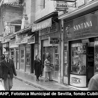 Aspecto de la plaza Jesús de la Pasión en 1977. Un espacio  que vemos ya invadido por los vehículos y que deja un corto espacio para los peatones. La óptica y tienda de fotografía Santana ubicada aún en la trasera de la iglesia del Salvador.  ©ICAS-SAHP, Fototeca Municipal de Sevilla, fondo Cubiles 